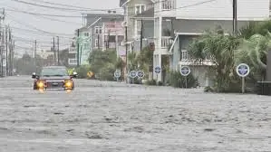 Car driving through hurricane flooding on a coastal street lined with raised homes